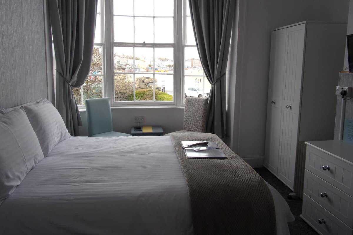 A hotel room with a bed, a desk, a chair, a wardrobe, and a window with curtains.