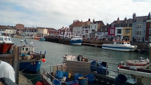 A harbor with boats docked, buildings along the waterfront, and a crowd of people. - The Cavendale (Weymouth)