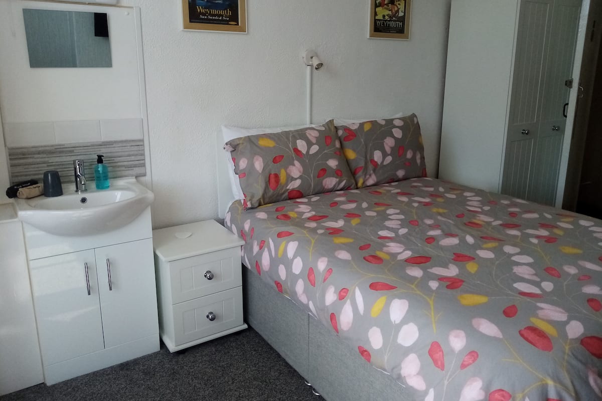 A bedroom with a bed, a nightstand, a sink, and a wardrobe.