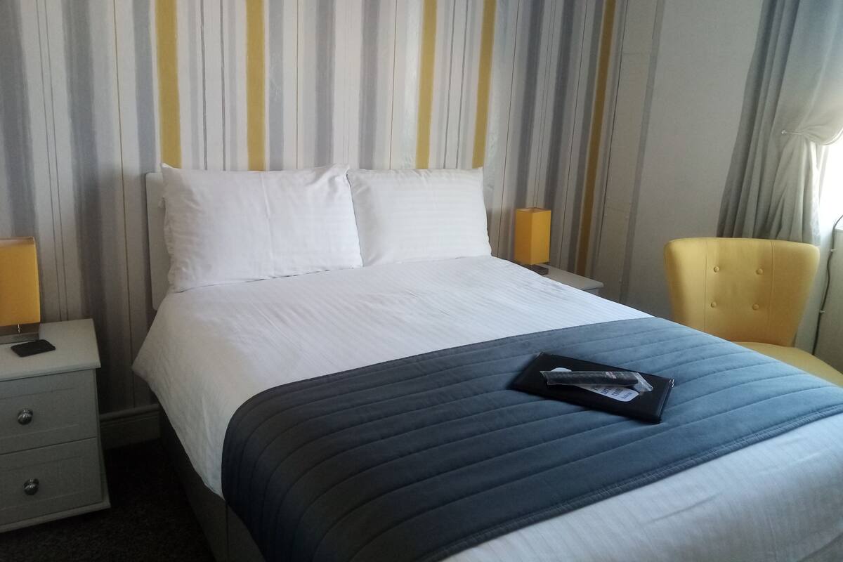 A hotel room with a bed, a bedside table, a chair, and a striped wall.