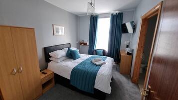 Ein Hotelzimmer mit Bett, Holzschrank, Nachttisch, Fernseher und einem Vorhangfenster.
