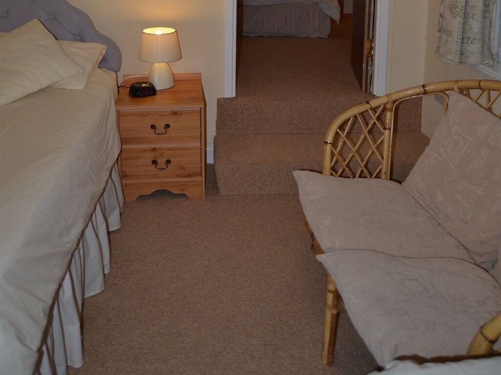 Een slaapkamer met een bed, een nachtkastje met een lamp, een houten nachtkastje en een rieten stoel.
