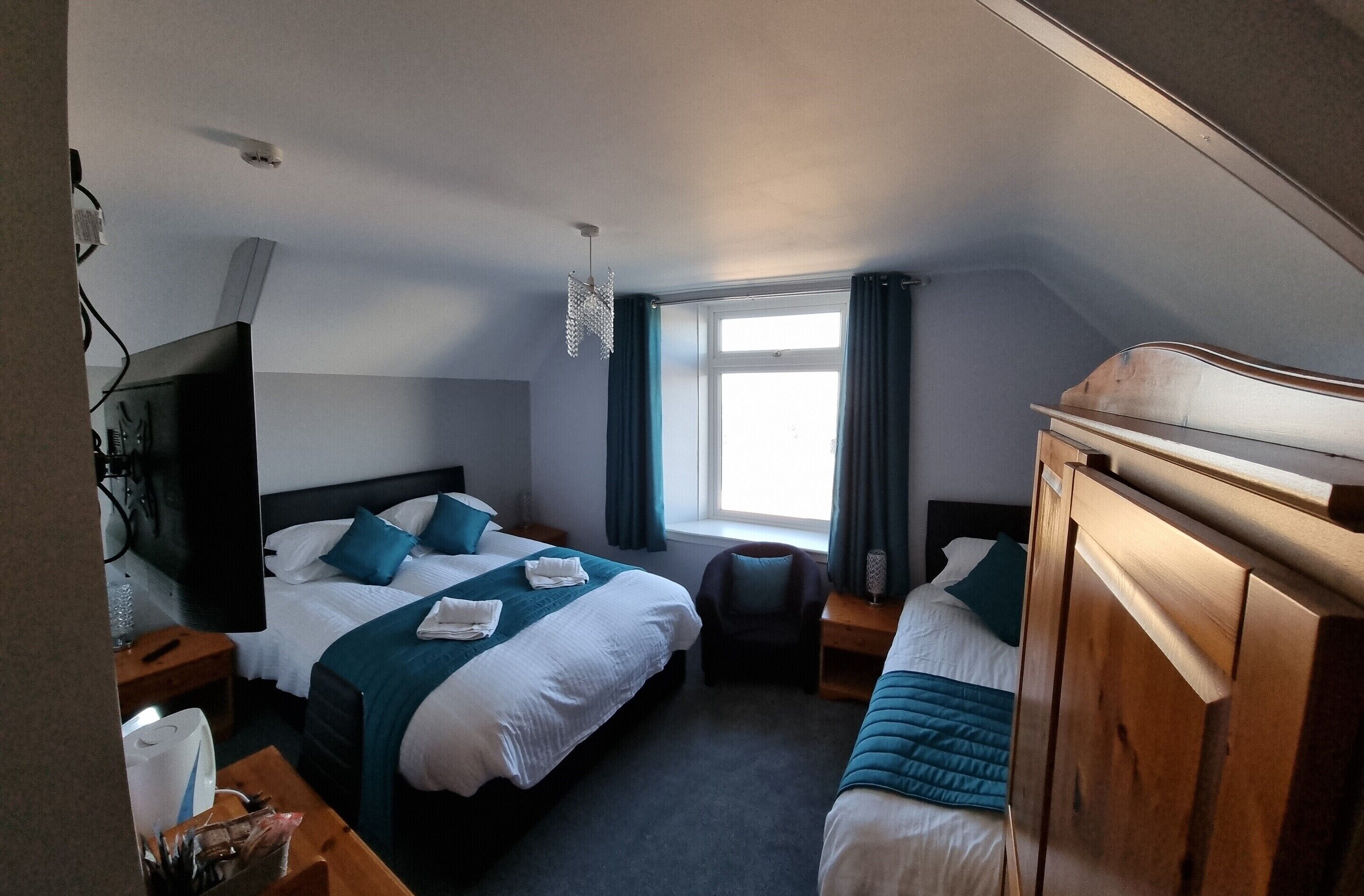 A hotel room with two beds, a TV, a window with curtains, a wooden headboard, and a small table with a lamp.