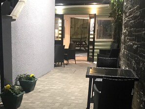 An outdoor patio area with a table and chairs, potted plants, and a brick wall.