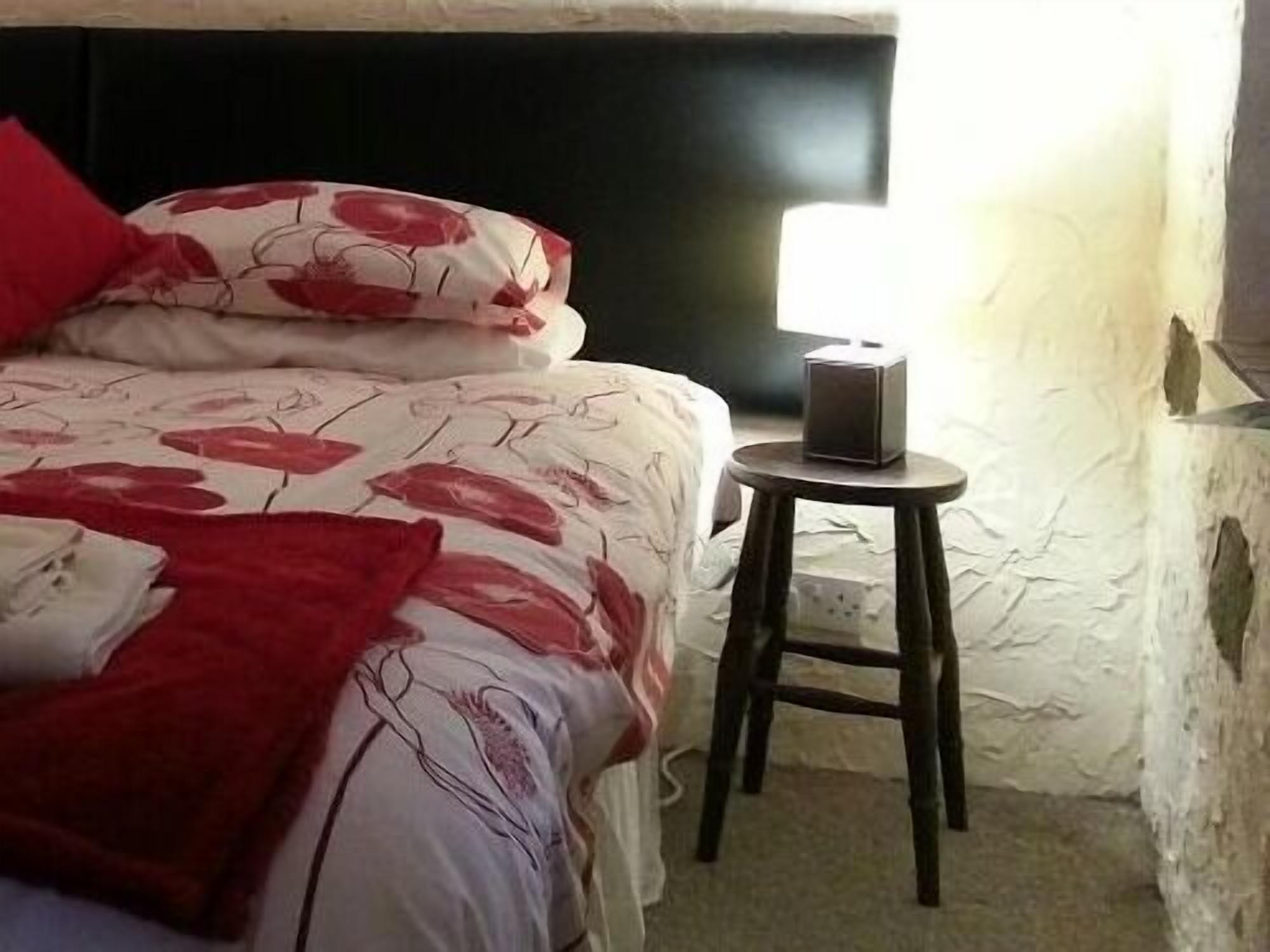Un dormitorio con cama, almohadas, mesita de noche y lámpara de pared.