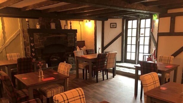 A cozy restaurant interior with wooden tables and chairs, a fireplace, and a staircase leading to an upper level. - The Crown Inn (Rhayader)