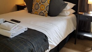 A neatly made bed with white linens, a patterned throw blanket, and a remote control on the side. - The Crown Inn (Rhayader)
