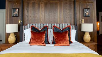 Una cama grande con cabecera de madera, dos mesitas de noche con lámparas y dos cuadros enmarcados en la pared.