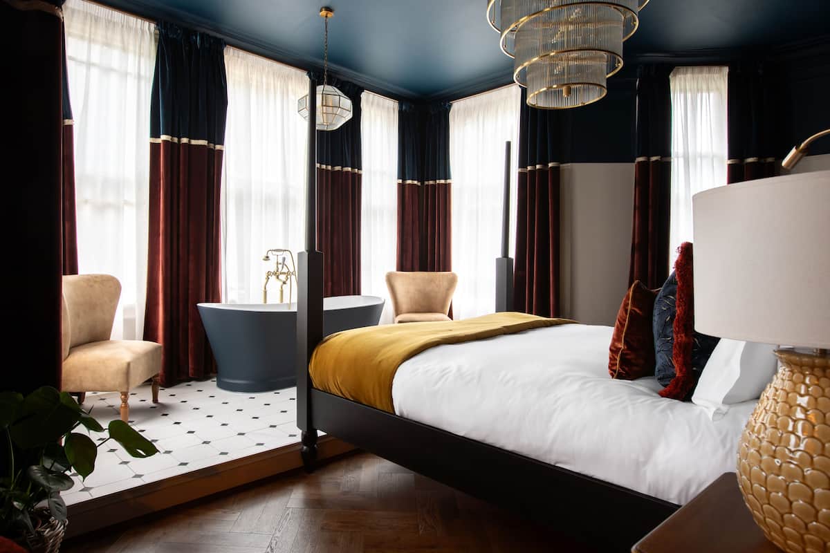 Una habitación de hotel moderna con una cama grande, dos sillones, una mesita y una bañera.