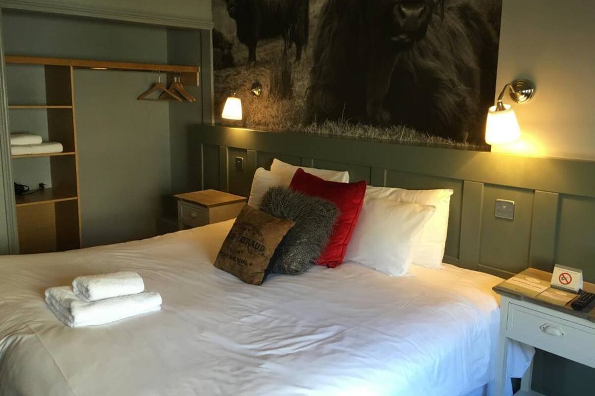 Una habitación de hotel con una cama grande, un armario, una mesita de noche y una lámpara de pared.