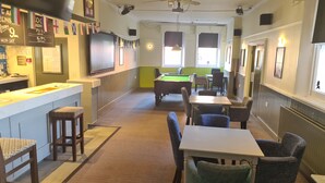 A billiards room with a pool table, chairs, and a bar area with a television. - Swan Hotel (Milton Keynes)