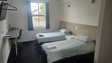 Una habitación pequeña y limpia con dos camas individuales, un escritorio y una silla.