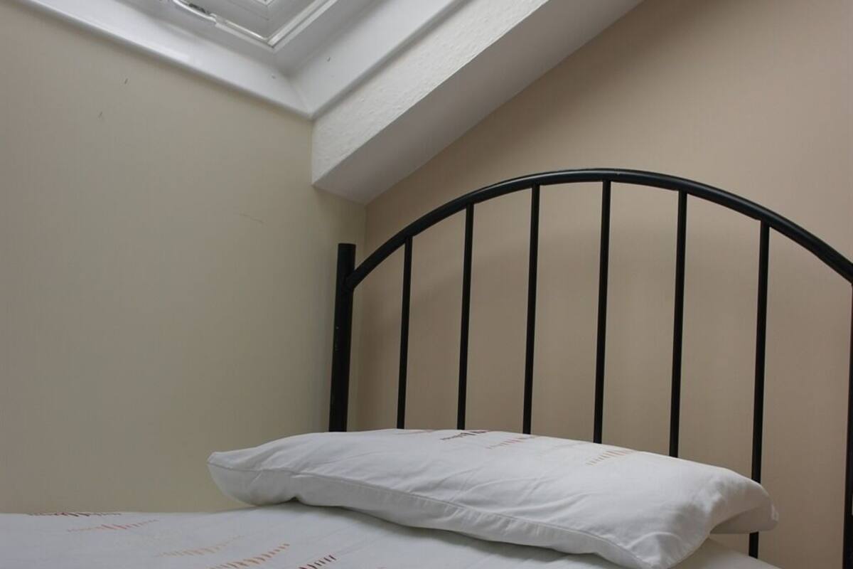 A single bed with a white mattress and pillow in a room with a sloped ceiling and a black metal headboard.
