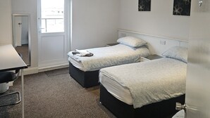 A hotel room with two beds, a desk, and a door leading to the outside. - Swan Hotel (Milton Keynes)