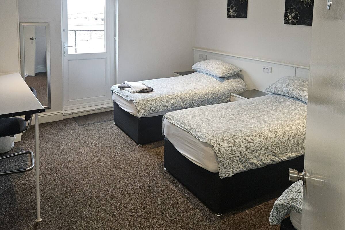 A hotel room with two beds, a desk, and a door leading to the outside.