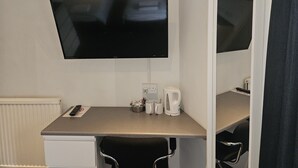A hotel room with a flat-screen TV mounted on the wall, a small table with a coffee maker, and a chair. - Swan Hotel (Milton Keynes)