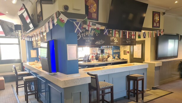 A bar area with a blue counter, stools, and flags. - Swan Hotel (Milton Keynes)