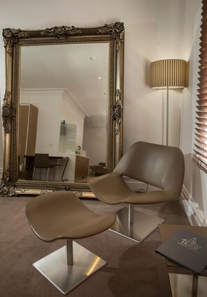 A modern room with a large ornate mirror, a contemporary chair, a lamp, and a small table with a book. - The Ikon Hotel (Burnie)