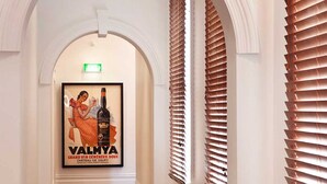 Corredor com um quadro de vinho Valmy, paredes brancas e venezianas de madeira.