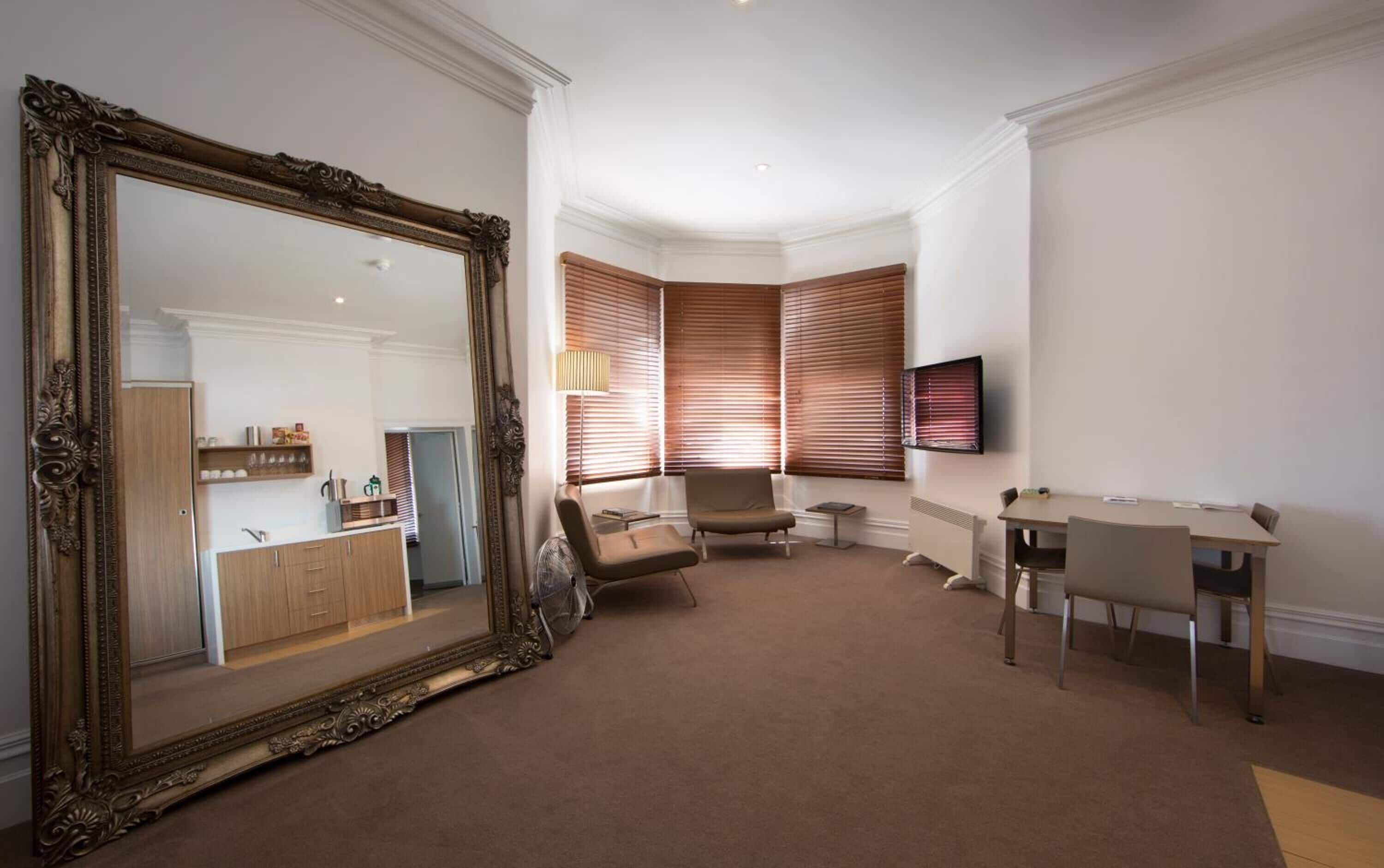A living room with a large ornate mirror, a seating area with a chair and a table, and a television mounted on the wall.