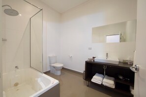A modern bathroom with a glass-enclosed shower, a white toilet, a sink with a mirror, and a shelf with towels. - The Ikon Hotel (Burnie)
