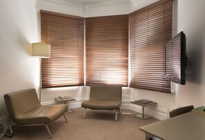 A corner room with a beige chair, a small table, and a TV mounted on the wall. - The Ikon Hotel (Burnie)
