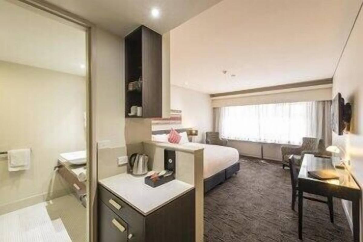 A hotel room with a bed, a desk, a chair, a wardrobe, and a window.