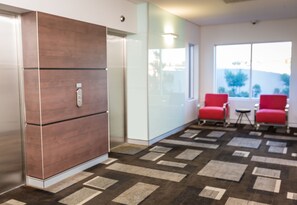 A modern room with a large brown cabinet, a glass partition, and a patterned carpet. There are two red chairs and a small table.