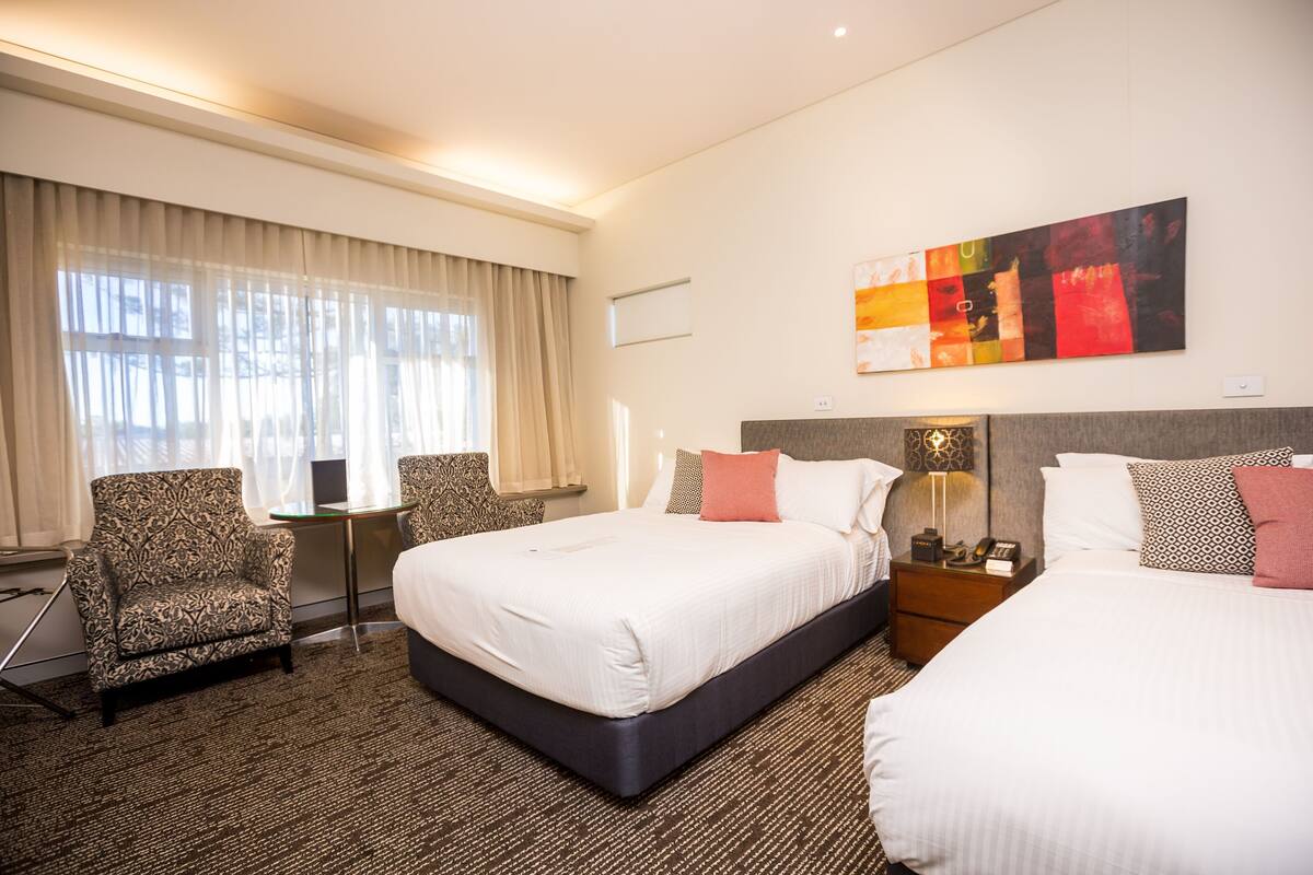 A hotel room with a large bed, two bedside tables, a chair, a desk, and a window with curtains.