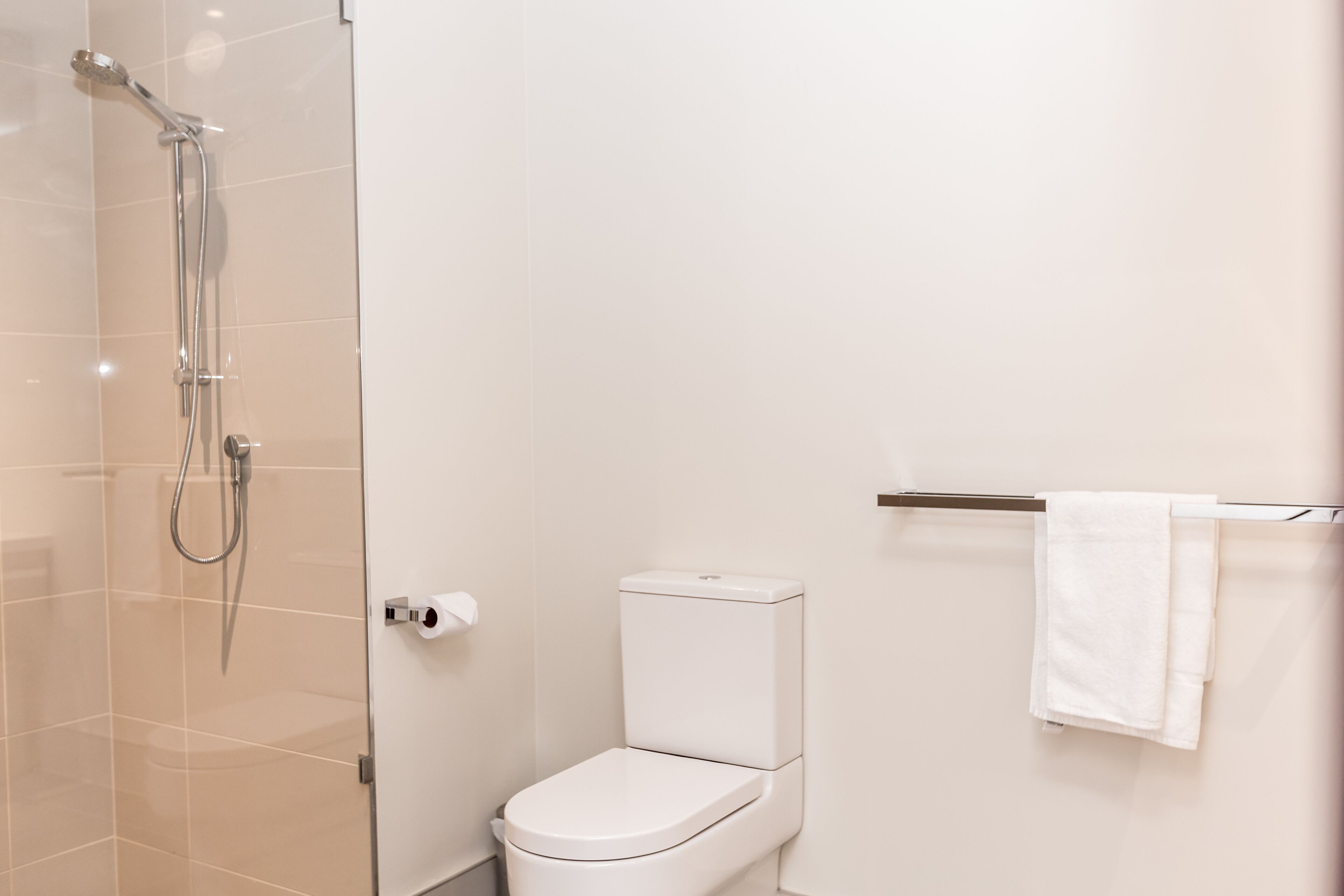 A modern bathroom with a glass shower enclosure, a white toilet, and a towel rack with a white towel.