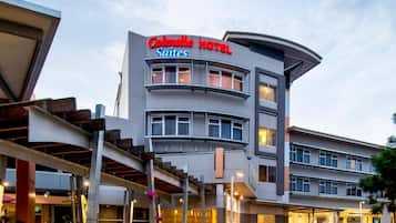 Ein modernes Hotel mit einem gut sichtbaren Schild, auf dem "Colmby Hotel Suites" steht. Es verfügt über einen mehrstöckigen Bau mit einer gewölbten Dachlinie und mehreren Balkonen. Der Eingang ist über einen überdachten Gang mit Pflanzkübeln zugänglich.