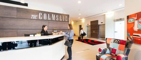A reception area with a sign reading "The Colmslie," a receptionist, and a colorful chair.