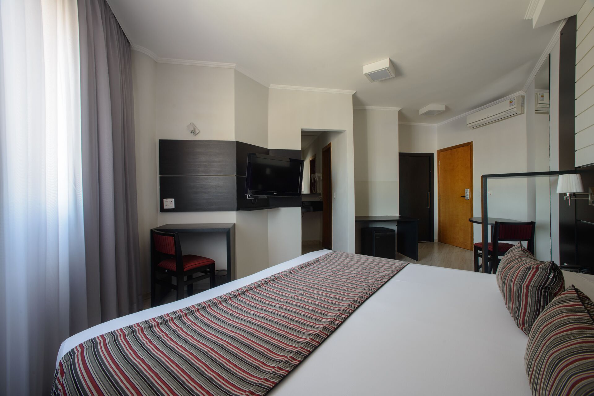 Une chambre d’hôtel moderne dotée d’un grand lit, d’un bureau avec une chaise, d’un téléviseur fixé au mur et d’un appareil de climatisation.