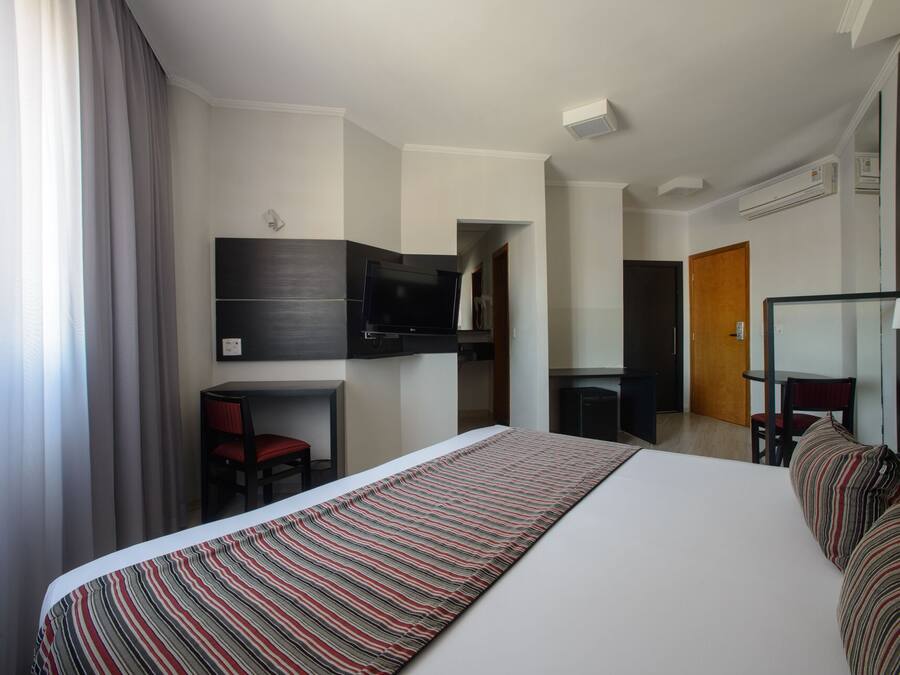Une chambre d’hôtel moderne dotée d’un grand lit, d’un bureau avec une chaise, d’un téléviseur fixé au mur et d’un appareil de climatisation.