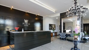 Un hall d’accueil d’hôtel moderne, avec un comptoir noir, un lustre et un grand miroir.