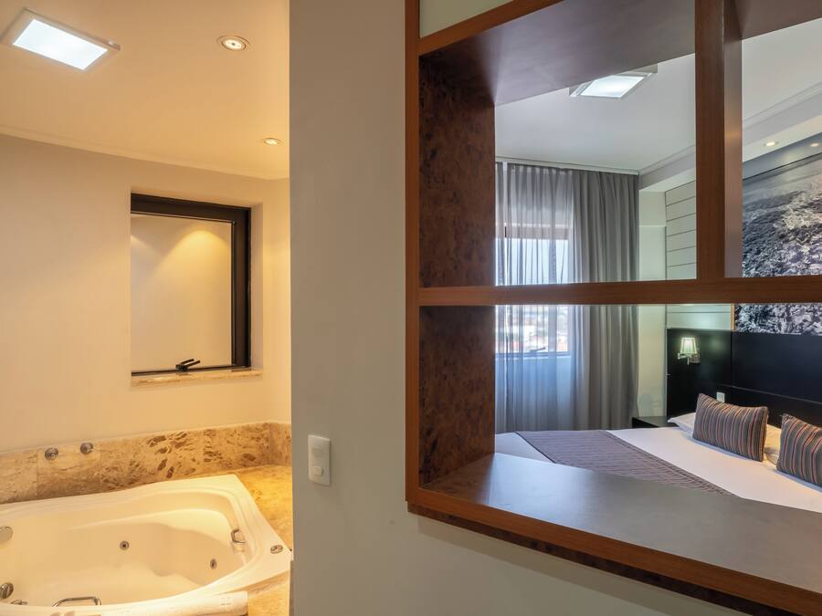 Una habitación de hotel moderna con una cama grande, un baño separado con bañera y un espejo grande que refleja la habitación.