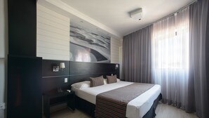 Une chambre d’hôtel avec un grand lit, une table de chevet, un téléviseur fixé au mur et une fenêtre avec des rideaux.