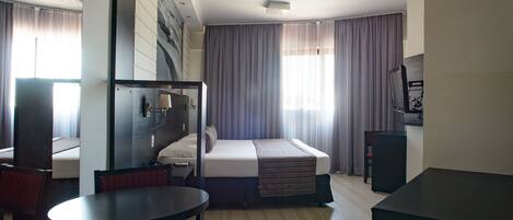 A hotel room with a bed, a desk, a chair, a TV, and a window with curtains.