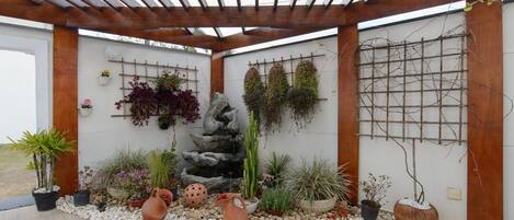 A covered outdoor area with a stone waterfall, potted plants, and a pergola structure.