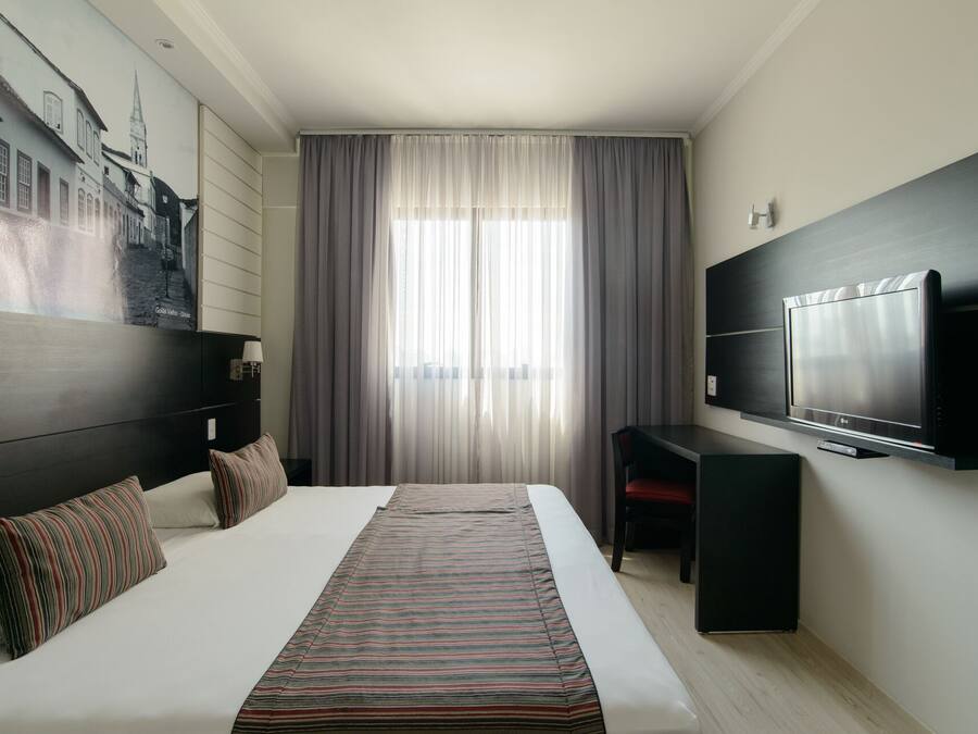 Una habitación de hotel moderna con una cama grande, un televisor de pantalla plana en la pared y un cuadro de un paisaje urbano.