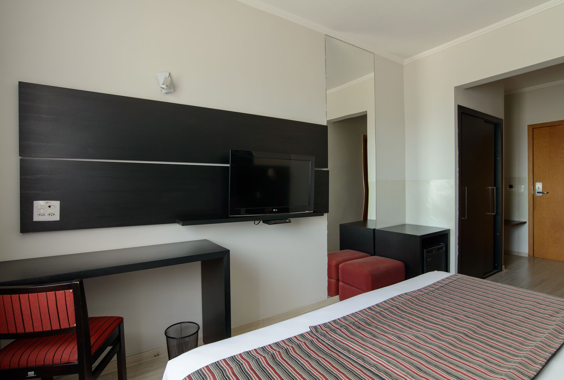 Una habitación de hotel moderna con una cama, un escritorio, un televisor y una silla roja.