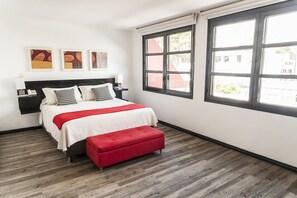 Une chambre à coucher avec un lit, un banc rouge et une fenêtre donnant sur des immeubles.