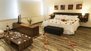 Una habitación de hotel con una cama, una mesita de noche, una mesa auxiliar, un sofá, un televisor y una planta.
