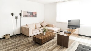 Una sala de estar moderna con un sofá color beige, una mesa de centro de madera, un televisor y una lámpara de pie.