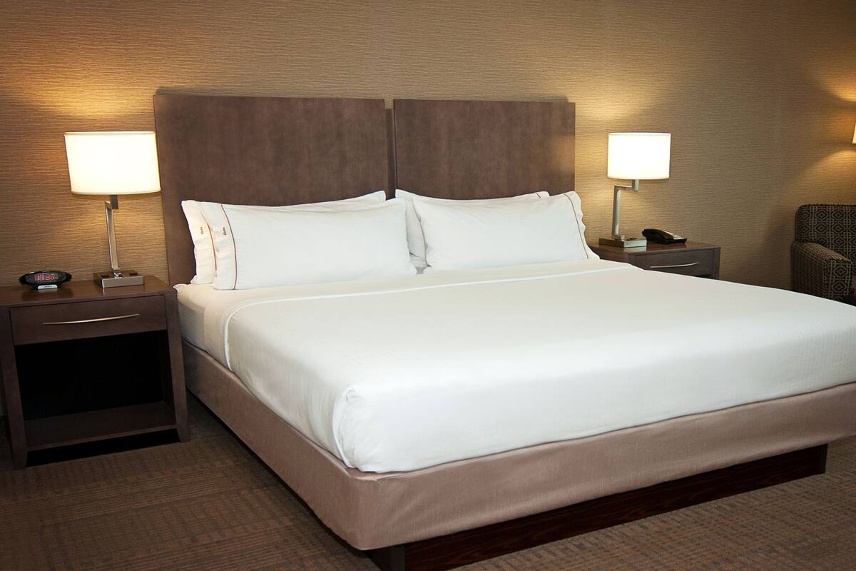 Habitación de hotel con una cama grande, dos mesitas de noche, una silla y dos lámparas de pared.