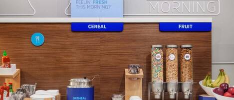 A breakfast bar with labeled sections for cereal and fruit, a blue oatmeal container, and a variety of condiments and utensils.