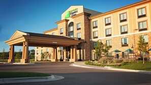 A hotel with a covered entrance, multiple windows, and a landscaped area with greenery. - Holiday Inn Express & Suites Wichita Northeast by IHG (Wichita)