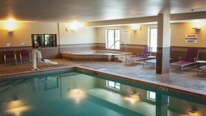 An indoor swimming pool with a hot tub, lounge chairs, and a lifeguard warning sign.