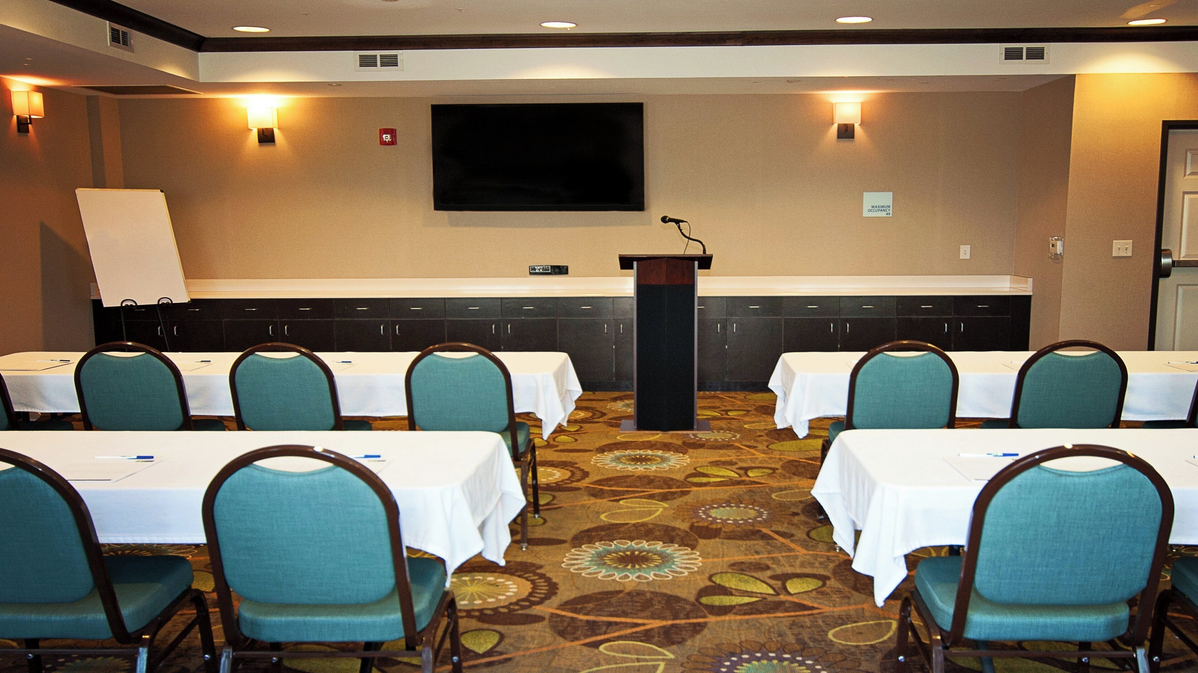 A conference room with tables, chairs, a podium, and a TV screen.