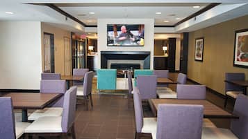 A restaurant with multiple tables and chairs, a television mounted on the wall, and a fireplace.